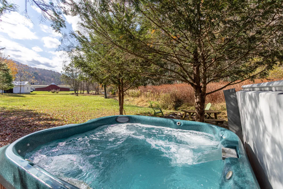 This image shows a spacious deck equipped with a hot tub and a picnic table, surrounded by lush trees. The deck is well-suited for relaxation and outdoor dining, with ample space for groups to gather and enjoy nature. The tranquil setting emphasizes the connection to the outdoors and the appeal of stargazing or sharing meals in a serene mountain environment.