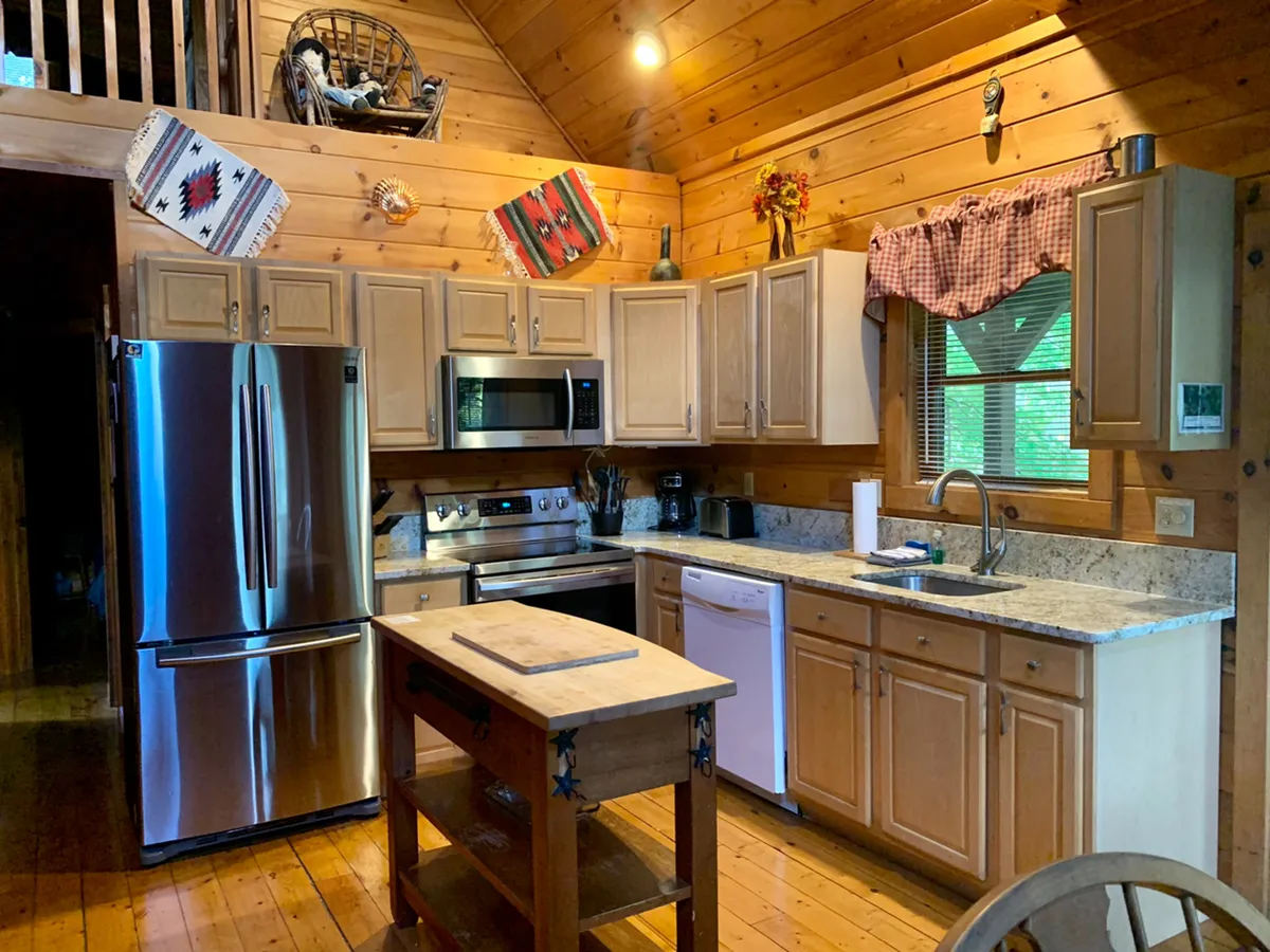 The kitchen area with stainless steel appliances, a central island for gathering or prepping meals, wooden cabinets, and decorative textiles, all illuminated by soft, inviting light. The setup suggests a space ready for socializing and family meal preparation.