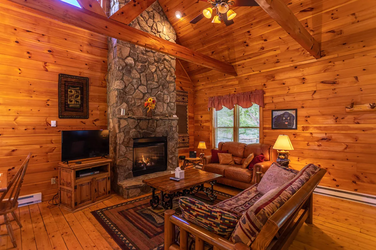 A spacious living room with a dramatic stone fireplace as the central feature, surrounded by wooden beams and comfortable seating arranged for conversation or relaxation. The area is bathed in warm natural light, and whimsical décor adds playful touches to the inviting atmosphere.