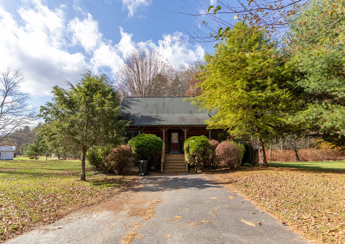 A broad exterior shot of the front of the cabin, featuring a landscaped yard, welcoming front porch, and a driveway. The paved access is clearly visible, hinting at the ease with which guests can come and go, especially to the nearby golf course.