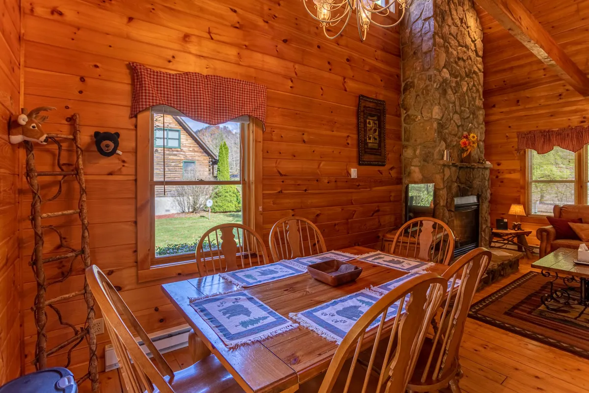 A warm, rustic dining space highlighted by a wooden table and a stone fireplace. A large window offers a glimpse of the outside, suggesting opportunities for gathering and celebrating after days spent exploring local activities.