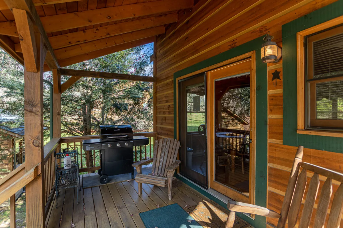 An inviting wooden deck equipped with a grill and comfortable chairs, perfect for outdoor dining or socializing. The natural surroundings and cozy setup offer a glimpse into post-golf relaxation and communal gatherings.