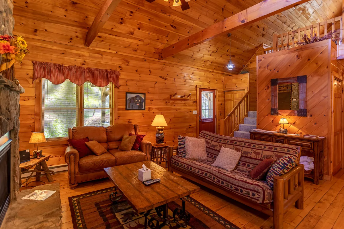 A cozy living area featuring wooden furniture, a prominent stone fireplace, and large windows that frame mountain scenery. Textile patterns and warm tones evoke comfort, while the open layout suggests space for family gatherings after a day outdoors.